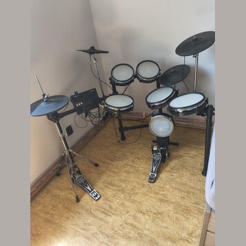 Elektronická bicí souprava s černým rámem a bílými bubnovými plochami. Souprava obsahuje pět padů, tři činely a ovládací modul s nápisem Roland. K sa…