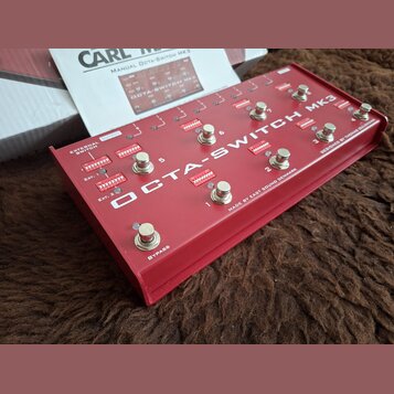Červený přepínač s nápisem OCTA-SWITCH MK3 a doplňkovými texty EXTERNAL SWITCH, EXT., EXT. 2, OUTPUT, BYPASS a MADE BY EAST SOUND DENMARK DESIGNED BY…