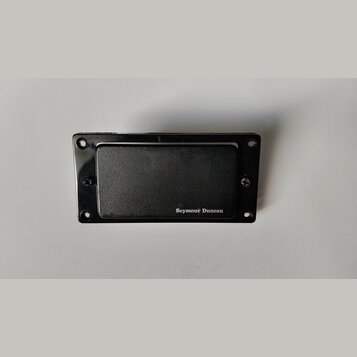 Černý kytarový snímač s krytem. V pravém dolním rohu je bílý nápis Seymour Duncan. Snímač je umístěn v černé rámečku s otvory pro šrouby. Povrch kryt…