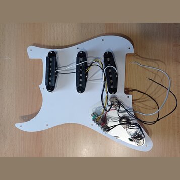 Bílá pickguard pro elektrickou kytaru s třemi černými snímači typu single-coil. K snímačům vedou bílé a černé vodiče, které jsou připojeny k elektron…