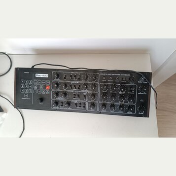 Černý analogový syntetizátor s nápisy Pro-800 a behringer. Přístroj obsahuje početné otočné knoflíky, tlačítka s čísly 0–9 a různé ovládací sekce jak…