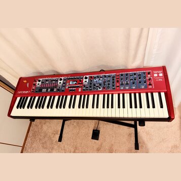 Červený digitální klavír Nord Stage 3 umístěný na černém stojanu. Na levé straně je bílý nápis nord Stage 3 a pod ním menší text ORGAN PIANO SYNTH SE…