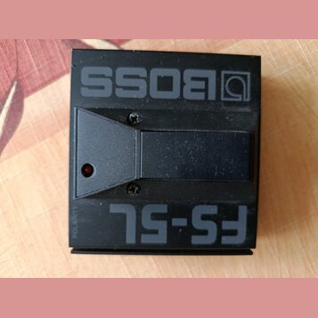 Černý nožní spínač z plastu s nápisy BOSS a FS-5L. Na levé straně je umístěna malá červená kontrolka a svislý nápis POLARITY. Povrch je matný s vidit…