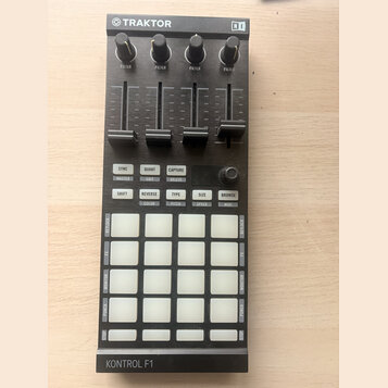 Černý MIDI kontrolér s nápisy TRAKTOR a NI v horní části. Zařízení obsahuje čtyři posuvníky s označením FILTER, pět řad bílých podsvícených tlačítek…