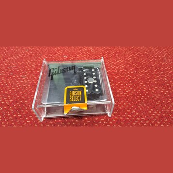 V průhledném plastovém boxu se nachází černý elektrický kytarový snímač. Na povrchu je vidět bílé logo Gibson a žlutá nálepka s nápisem GIBSON SELECT…