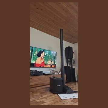 Černý reproduktorový systém složený z vysokého sloupového reproduktoru a subwooferu. Na přední straně subwooferu je bílý nápis JBL. V pozadí jsou vid…