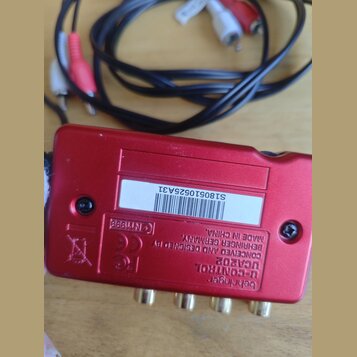 Červené kovové zařízení s nápisy behringer U-CONTROL UCAR02 CONCEIVED AND DESIGNED BY BEHRINGER GERMANY. MADE IN CHINA. Na spodní straně je bílá nále…
