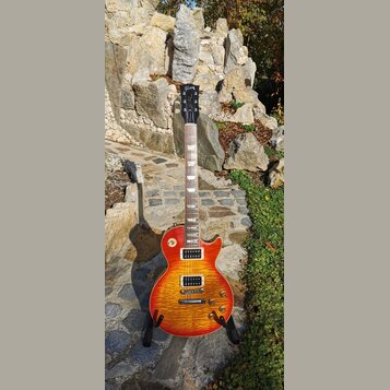 Elektrická kytara s tělem v žlutě-oranžovém gradientu (sunburst) a viditelnou strukturou dřeva. Na hlavě je bílý nápis Gibson a podpis v kurzivě. Kyt…