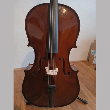 Hnědý smyčkový nástroj, pravděpodobně violoncello, s lakovaným povrchem. Na těle jsou vidět f-otvory, světlá dřevěná kobylka a černý strunník. Nástro…