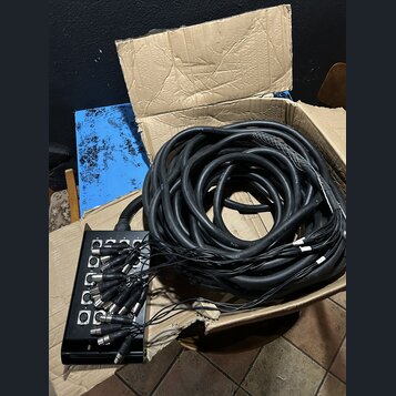 Černá stagebox s osmi vstupy XLR, ze kterých vychází svazek černých kabelů. V horní části stageboxu jsou viditelné nápisy 1 až 8 u jednotlivých vstup…