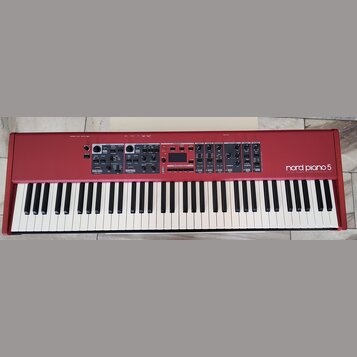 Červený digitální klavír s bílými a černými klávesami. Na pravé straně je bílý nápis nord piano 5 a pod ním menší text VIRTUAL HAMMER ACTION TECHNOLO…