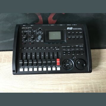 Černý digitální sekvenční přístroj značky ZOOM, model R8 s nápisem Recorder:Sampler Interface:Controller. Zařízení obsahuje displej, několik ovládací…