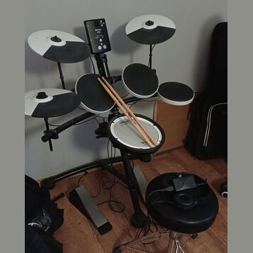 Elektronická bicí souprava s černým rámem a bílo-černými činely. Na modulu je viditelné logo Roland a označení TD-1. Na snareu je nápis Roland, na pa…