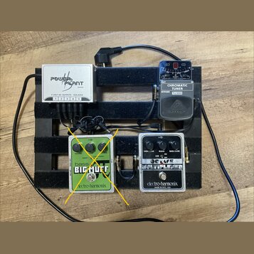 Na černém pedalboardu jsou umístěny čtyři efekty a napájecí zdroj. V horní části je bílý zdroj s nápisem POWER PLANT Junior a pětivstupním rozdělením…