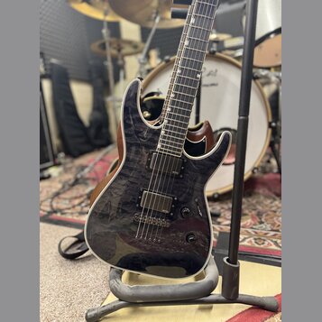 Elektrická kytara s tmavým, žilnatým povrchem těla a hnědými hranami. Nástroj má dva humbuckery s nápisem emo a tři ovládací knofíky. Kytara je umíst…