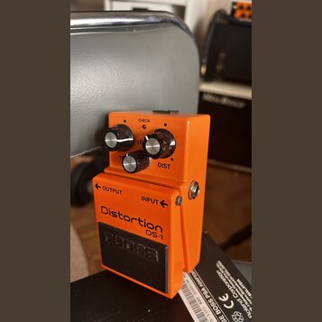Oranžový kytarový efekt s nápisy Distortion DS-1 a logem BOSS na spodním černém pedálu. Na horní části jsou tři ovládací knoflíky s popisky LEVEL, DI…