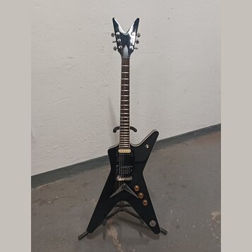 Černá elektrická kytara s tělem ve tvaru hvězdy a chromovanou hlavou. Na hlavě je viditelné logo DEAN. Kytara má dva humbuckery, tři ovládací knoflík…