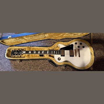 Bílá elektrická kytara s tvarem single-cut v černém kufru s žlutým vnitřkem. Na hlavě je logo Epiphone a nápis "Elite". Kytara má dva humbuckery, zla…