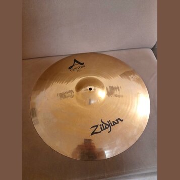 Zlatavý kovový činel s viditelným broušením povrchu. Na činely jsou černé nápisy Zildjian a CUSTOM A, pod kterým je menší text RIDE 20"/0750. Povrch…