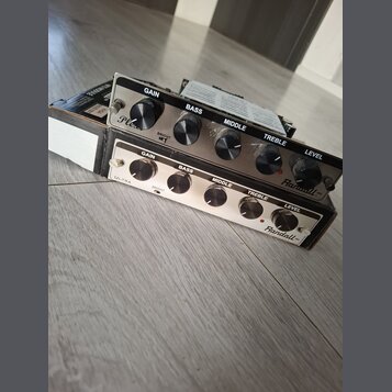 Dvě kytarové zesilovače s kovovým předním panelem a černými ovládacími knoflíky. Horní jednotka má nápisy GAIN, BASS, MIDDLE, TREBLE, LEVEL a logo Ra…