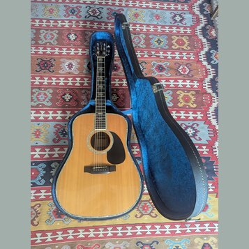 Akustická kytara s přírodním dřevem a černým plechtrem v modrém tvrdém pouzdře. Na hlavě nástroje je viditelné logo "Epiphone". Kytara i pouzdro vyka…