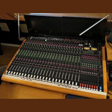 Velký míchací pult s dřevěným rámem a černým ovládacím panelem. Na pravé straně je nápis TOFT AUDIO CONSOLE MTO a logo Toft Audio Design. Panel obsah…