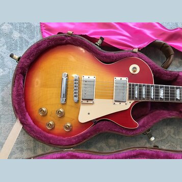 Elektrická kytara s tónem sunburst (červená a žlutá) v hnědém kufru s fialovou výstýlkou. Nástroj má dva humbuckery, čtyři zlaté ovládací knoflíky a…