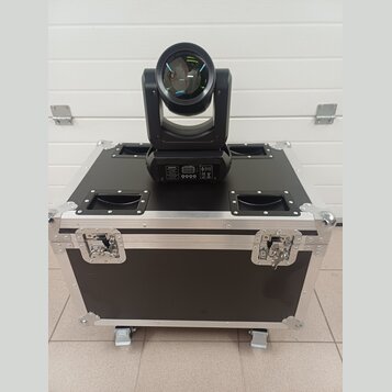 Černý světelný efekt typu moving head umístěný na černé transportní bedně s hliníkovými hranami a úchyty. Na zadním panelu efektu je viditelný disple…