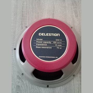 Reproduktor s růžovým magnetem a šedým kovovým rámem. Na štítku je uveden nápis CELESTION a detaily: Model G12 H, Power capacity 150 WATTS, Impedance…