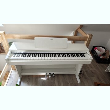 Bílé digitální piano s bílým stojanem a třemi pedály. Na hudebním stojanu je umístěno logo YAMAHA. Nástroj vykazuje čistý povrch bez viditelných pošk…