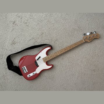Červená elektrická basová kytara s bílým pickguardem a světlou hnedou hmatníkem. Na hlavě nástroje je viditelné logo "Randy Bass". Kytara má čtyři st…