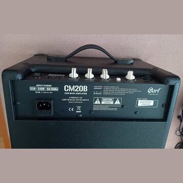Zadní strana černého basového komba s nápisem CM20B 20W BASS AMPLIFIER a logem Cort. Na štítku je uveden vstupní napětí 220-240V~50/60Hz a Serial Num…