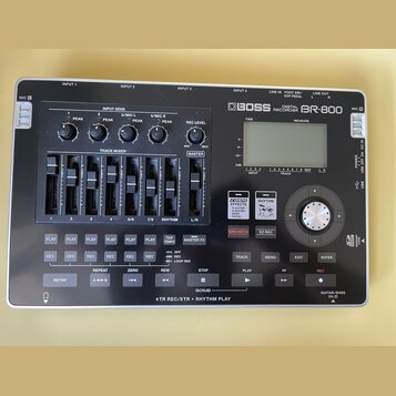 Stříbrnošedý digitální nahrávač s černým ovládacím panelem. Na horní části je nápis BOSS DIGITAL RECORDER BR-800 a LCD displej. Přístroj obsahuje něk…