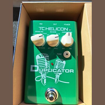 Zelený efekt pedál s nápisem TC HELICON a DUPLICATOR. Na horní straně jsou tři bílé otočné ovladače s popisky DOUBLING (TIGHT, LOOSE), REVERB (RM, CL…