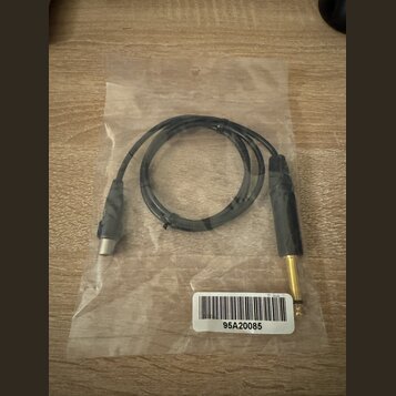 Černý audio kabel s konektory na obou koncích, umístěný v průhledném plastovém sáčku. Jeden konektor je zlatý jack, druhý je stříbrný. Na bílé nálepc…