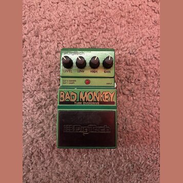 Zelený kytarový efekt s nápisy BAD MONKEY a TUBE OVERDRIVE. Na horní části jsou čtyři černé otočné ovířky s popiskem LEVEL, LOW, HIGH a GAIN. V horní…