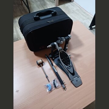 Na fotografii je černý basový pedál s logem Pearl na šlapce a doprovodný černý kufr. K pedálu jsou přiloženy volné části: beater s plstěnou hlavou, k…