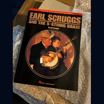 Kniha s černým obalem a červeným horním okrajem. Na předsłówce je nápis REVISED AND ENHANCED EDITION a název EARL SCRUGGS AND THE 5-STRING BANJO By E…