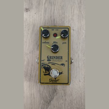 Kytarový efekt pedál v béžovém provedení s černými ovládacími knoflíky. Na povrchu jsou nápisy GRINDER, rat distortion a Gorhat pedals spolu s černým…