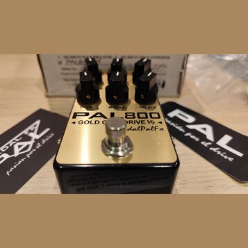 Kytarový efekt pedál s zlatým horním panelem a černým šasi. Na povrchu je nápis PAL800, GOLD Overdrive V4 a dalPalfx. Pedál má tři černé kontrolní kn…