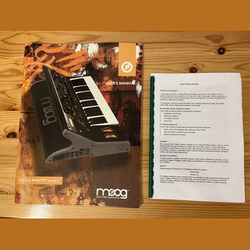 Fotografie zobrazuje uživatelskou příručku a doprovodný printed list v češtině k syntetizátoru. Na obálce manuálu je nápis USER'S MANUAL a v dolní čá…