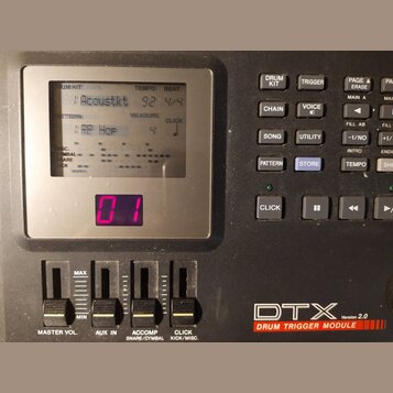Černý elektronický modul s displejem a ovládacími prvky. Na spodní části je bílý nápis DTX Version 2.0 a pod ním červený pruh s textem DRUM TRIGGER M…