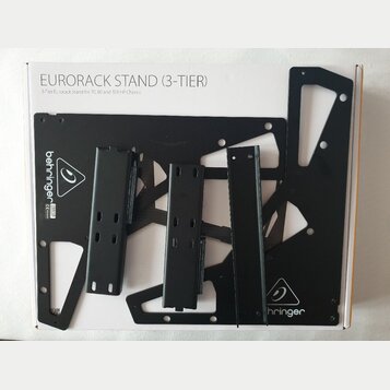 Bílá krabice s nápisem EURORACK STAND (3-TIER) a podtitulem 3-Tier Eurorack Stand for 70, 80 and 104 HP Chassis. Uvnitř jsou rozložené černé kovové d…
