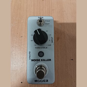 Stříbrný kytarový pedál s nápisy NOISE KILLER a MOOER. Obsahuje jeden černý otočný knoflík s označením THRESHOLD a hodnotami od -70 do +10dB, přepína…