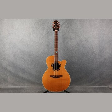 Akustická kytara s vyřezem (cutaway) v přirozené dřevěné barvě. Na hlavě je viditelné logo "Taylor". Hриф má v 12. poličce malý modrý ozdobný prvek.…
