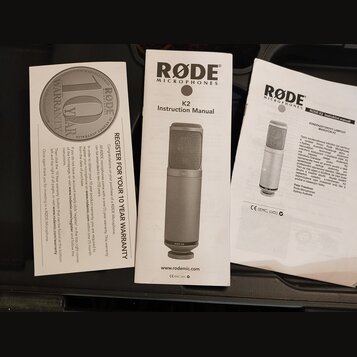 Fotografie zobrazuje tři papírové dokumenty k mikrofonu. Uprostřed je „K2 Instruction Manual“ od značky RØDE MICROPHONES s obrázkem stříbrného mikrof…