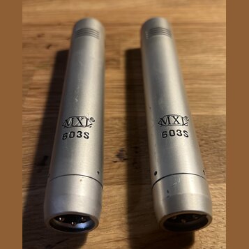 Dvě stříbrné kondenzátorové mikrofony s matným povrchem. Na obou je vyražen nápis MXL 603S. Povrch mikrofonů vykazuje drobné škrábance a známky použí…