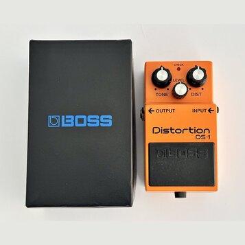 Oranžový kytarový efekt s černým spodním panelem a nápisy Distortion DS-1 a BOSS. Na horní části jsou tři černé otočné ovnovátka s popisky TONE, LEVE…
