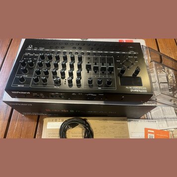 Černý syntetizátor Roland SYNTHESIZER SH-4d s velkým množstvím otočných knoflíků, posuvníků a ovládacích prvků. Na přední straně je viditelné logo Ro…