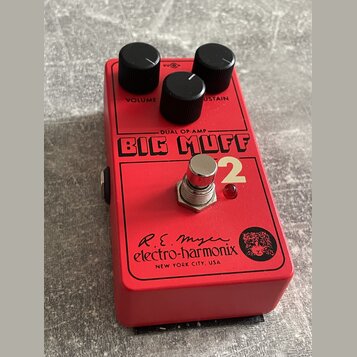 Červený kytarový efekt s nápisem BIG MUFF Pi 2 a DUAL OP-AMP. Na spodní části je logo electro-harmonix, podpis R.E. Myer a nápis NEW YORK CITY, USA s…